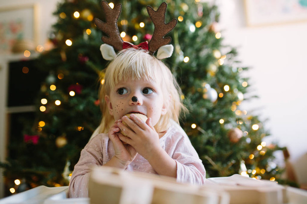 adorable petite fille portant des bois de Noël drôles et manger des biscuits, joyeuses vacances à la maison
 - Photo, image