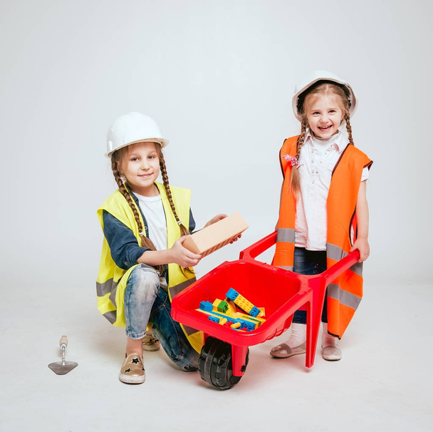 Two little cheerful girls with braids playing in repair or construction on white - Фото, зображення