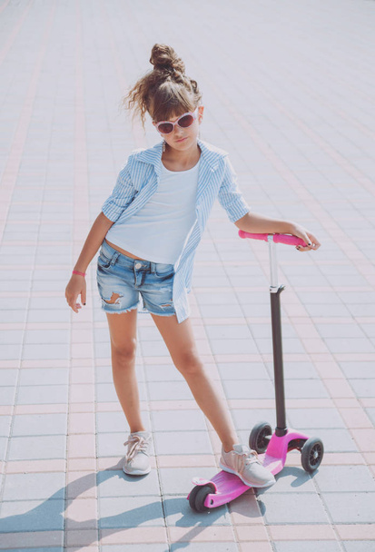 Little girl riding scooter on the street at sunny day - 写真・画像