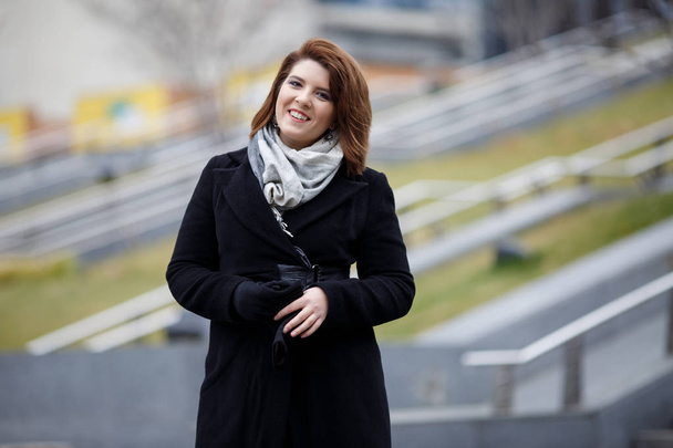 Photo of smiling brunette in black coat and scarf on blurred background - Photo, image