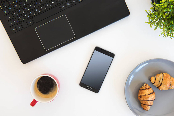 Top view of items on a table at office workstation. Flat lay with coffee and croissants. - Photo, Image