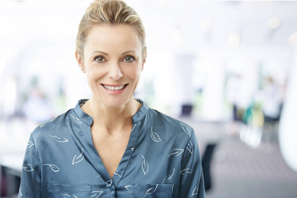 Close-up portrait of a happy middle aged businesswoman standing at the office. - 写真・画像