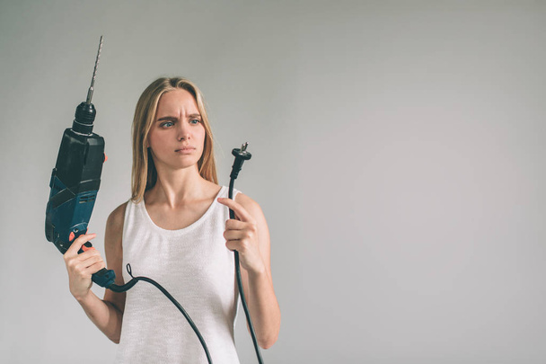 Funny portrait upset craftswoman. Blonde woman is wearing shirt isolated on white. Girl does not know how to use a drill - Foto, Bild