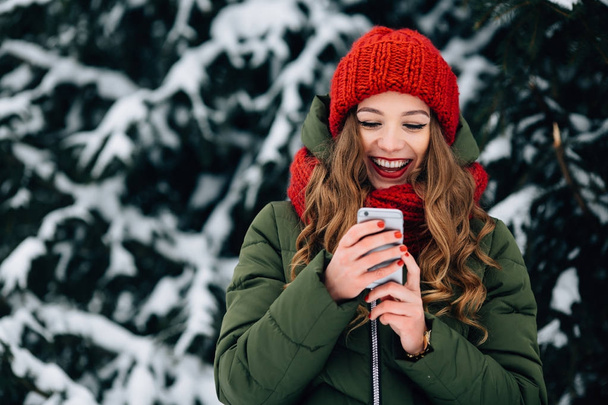 Girl in red winter hat and scarf using smartphone and smiling. - Foto, imagen