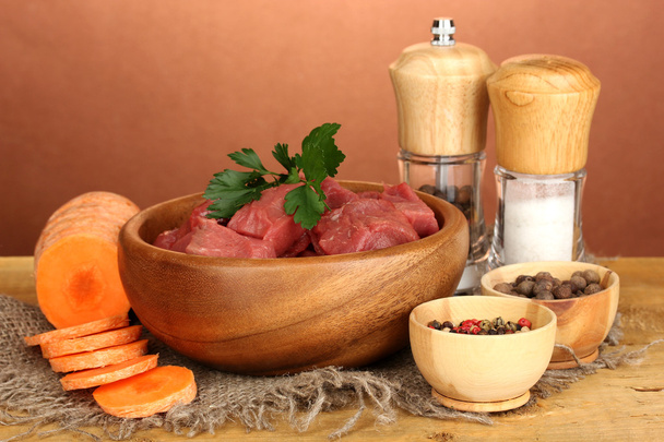 Raw beef meat marinated with herbs and spices on wooden table on brown background - Fotó, kép