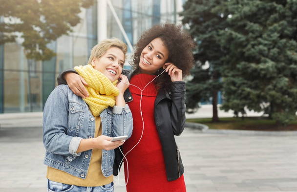 Happy female friends listen to music outdoors - Photo, Image
