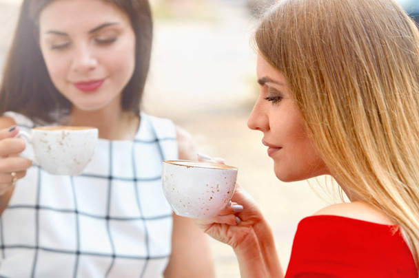 Attractive young women drink coffee in summer city - Photo, Image