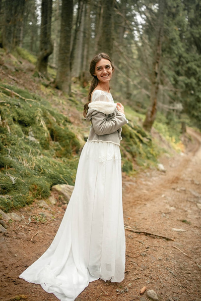 La novia se para en el camino del bosque, sonríe y mira hacia atrás
. - Foto, Imagen