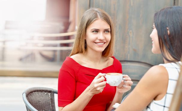 Attractive young women drink coffee in outdoor cafe - Zdjęcie, obraz