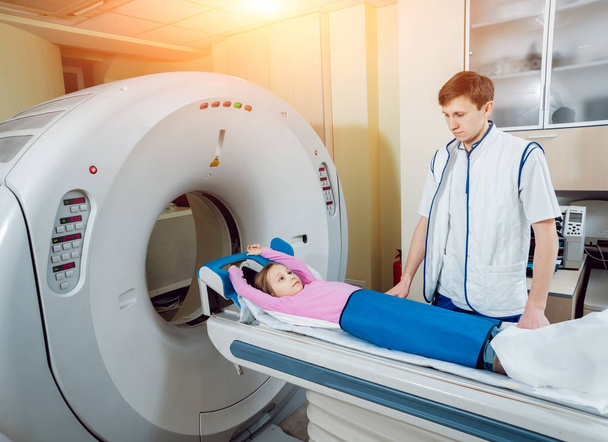 Medical equipment. Male caucasian doctor and little girl patient in room of computed tomography at hospital. - Photo, Image
