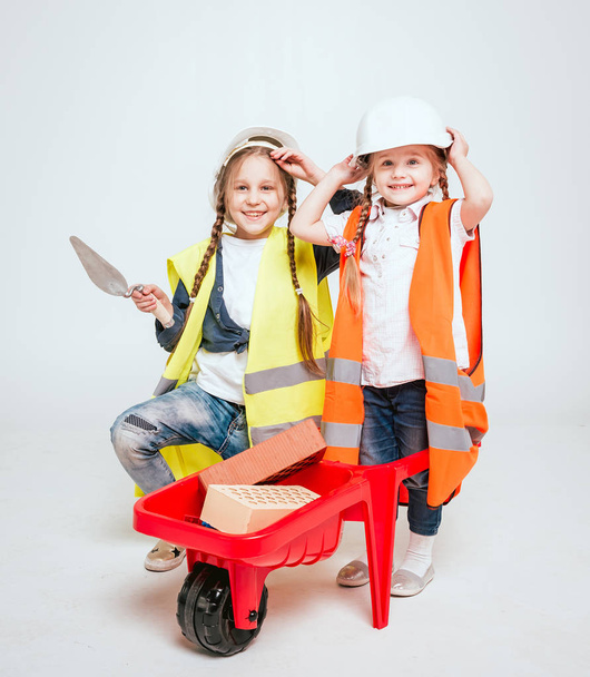 Two little cheerful girls with braids playing in repair or construction on white - Zdjęcie, obraz