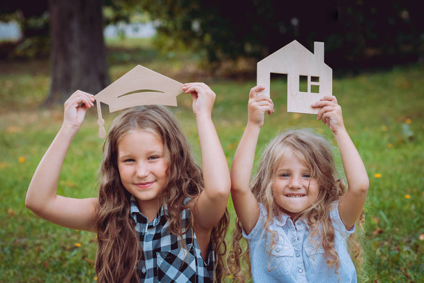 Two little girls with advertising signs graduate cap and house in park.  - Foto, imagen