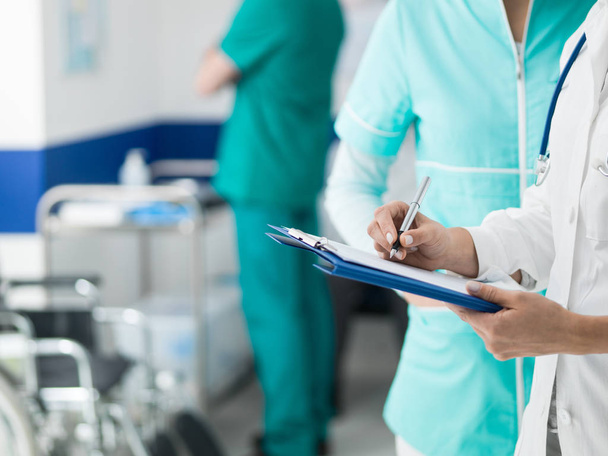 Medical staff working at the hospital: doctor and nurse checking a patient's medical record on a clipboard, healthcare and medical exams concept - Photo, Image