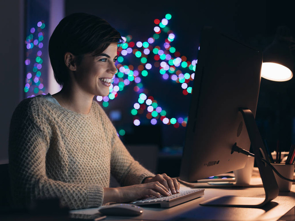 Feliz joven sonriente que conecta con su computadora tarde en la noche, ella está charlando y las redes sociales con sus amigos en línea
 - Foto, imagen