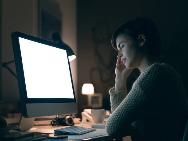 Tired young woman working with her computer late at night, she is leaning on her hand and sleeping with eyes closed - 写真・画像