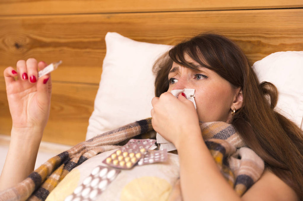 Mujer enferma en su cama mirando un termómetro clínico
 - Foto, imagen