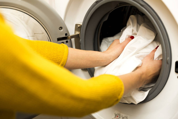 Женщина вручную загружает грязную одежду в стиральную машину
 - Фото, изображение
