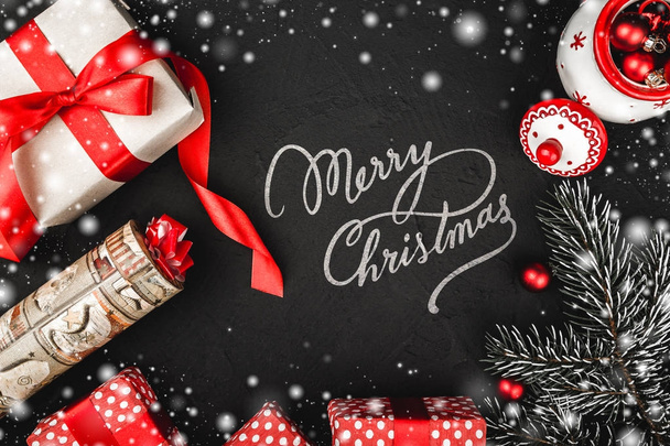 xmas aanwezig geschenkdozen, fir tak en rode boom globes op zwarte stenen achtergrond bekeken van boven, boven, besneeuwde wenskaart met Merry Christmas ondertekenen - Foto, afbeelding