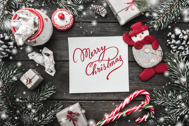 Motivační téma Vánoce, papíru s Merry Christmas signální, s červenou mašlí, jedle, současné krabic, glóby, ručně vyráběné sněhulák hračky dřevěné pozadí, pohled shora, blahopřání - Fotografie, Obrázek