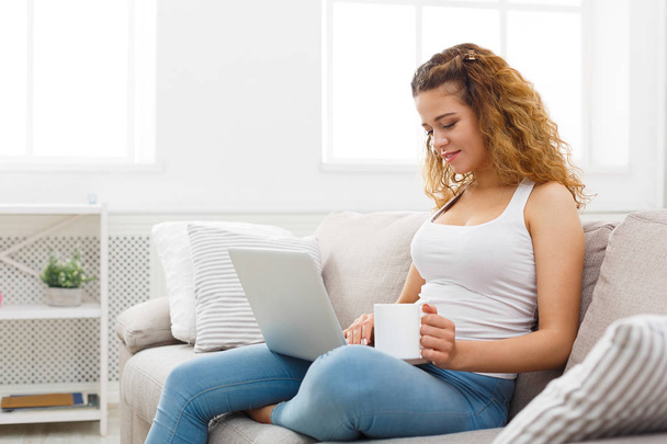 Chica joven con el ordenador portátil sentado en el sofá beige
 - Foto, imagen