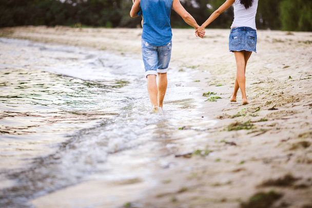 Vacaciones familiares cerca del mar. Dos adultos en ropa vaquera con un niño en sus brazos caminan por la playa de arena por detrás
 - Foto, imagen