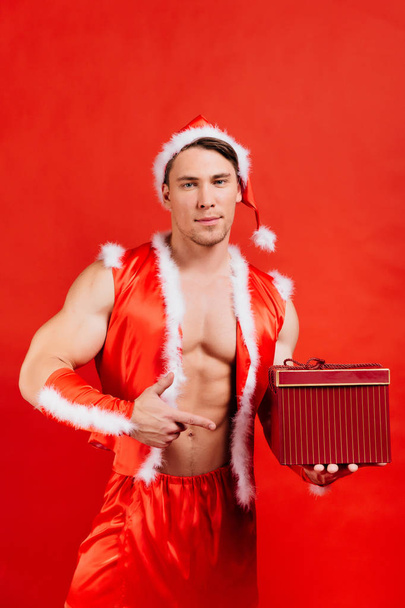 Holidays celebrations, New year, Christmas. Sexy fitness Santa Claus in a hat is holding a gift box. - 写真・画像
