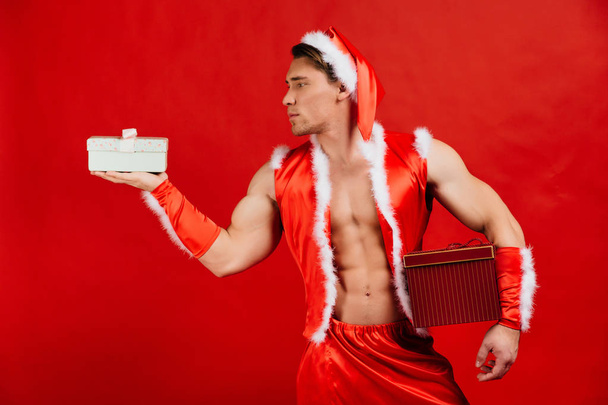 Holidays celebrations, New year, Christmas. Sexy fitness Santa Claus in a hat is holding a gift box. - Фото, зображення