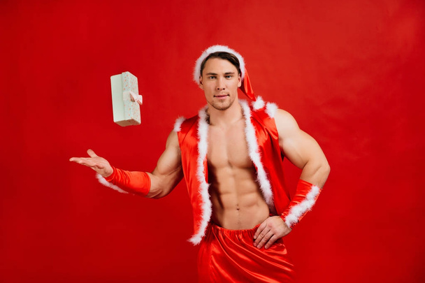 Tatil kutlamaları, yılbaşı, yılbaşı. Seksi fitness Noel Baba şapkalı bir hediye kutusu tutuyor. - Fotoğraf, Görsel