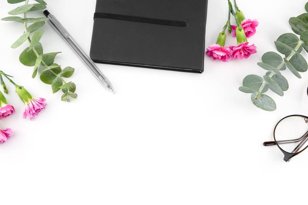 schwarzes Notizbuch und Gläser mit Baby-Eukalyptusblättern und rosa Nelkenblüten auf weißem Hintergrund mit Kopierraum - Foto, Bild