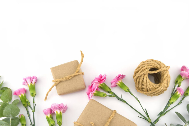 Kahverengi hediye kutuları ve bebek okaliptüs yaprakları ve kopya alanı beyaz zemin üzerine pembe karanfil çiçek ile dekore edilmiş halatlar - Fotoğraf, Görsel
