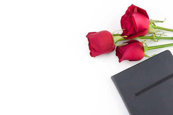 rote Rosen Strauß und schwarzes Notizbuch auf weißem Hintergrund mit Kopierraum - Foto, Bild