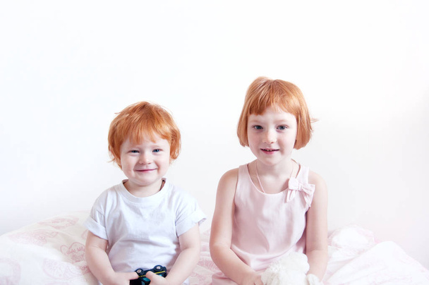 Red-haired brother and sister are sitting on the bed - Fotoğraf, Görsel