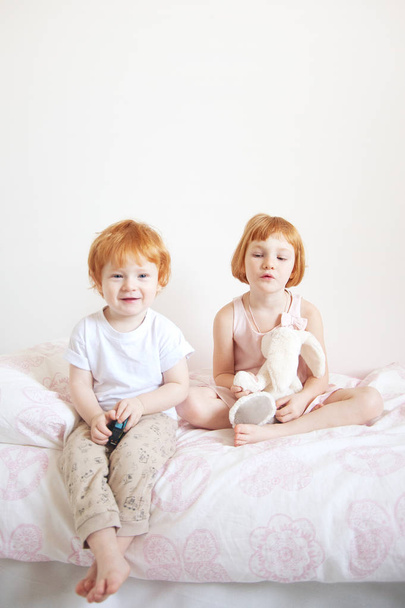 Red-haired brother and sister are sitting on the bed - Фото, изображение