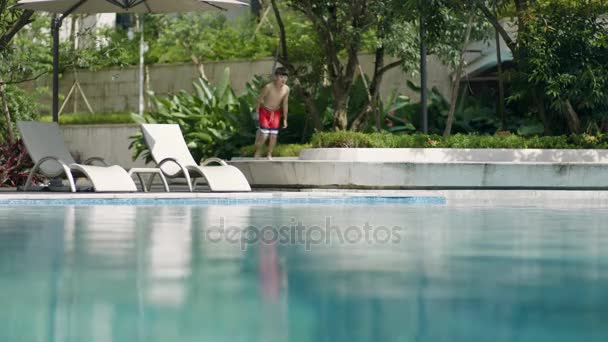 Азіатський підліток, біг і стрибки в плавальний басейн у саду повільний рух - Кадри, відео