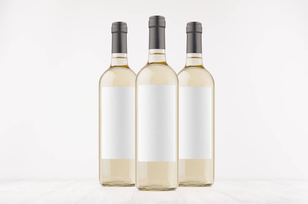 Three trasparent wine bottles with blank white labels on white wooden board, mock up. Template for advertising, design, branding identity. - Foto, Imagem