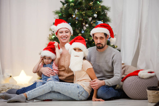 Picture of happy family in Santa caps at Christmas tree - Zdjęcie, obraz