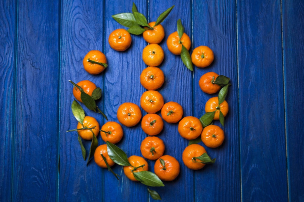 orange juicy mandarins (mandarins) with green leaves on a blue w - Foto, imagen