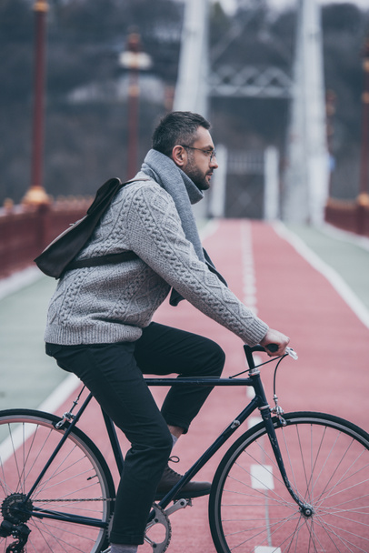 Zijaanzicht van knappe volwassen man fiets op voetgangersbrug - Foto, afbeelding