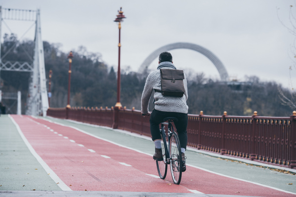 tyylikäs mies ratsastus polkupyörällä jalankulkijoiden sillalla syyspäivänä
 - Valokuva, kuva