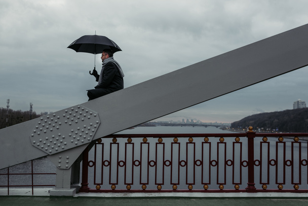hombre solitario con paraguas sentado en la construcción del puente
 - Foto, Imagen