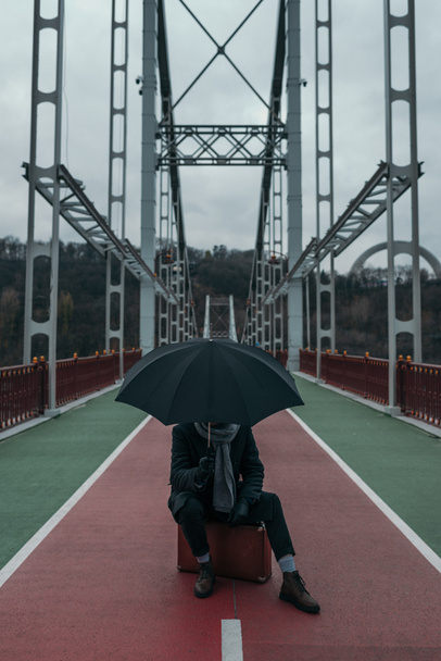 Stylowy mężczyzna z parasolem, siedząc na walizkę na most dla pieszych - Zdjęcie, obraz