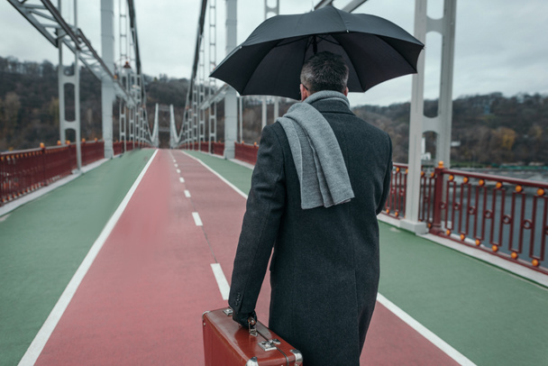 elegáns férfi esernyő és poggyász gyaloglás gyalogos híd - Fotó, kép