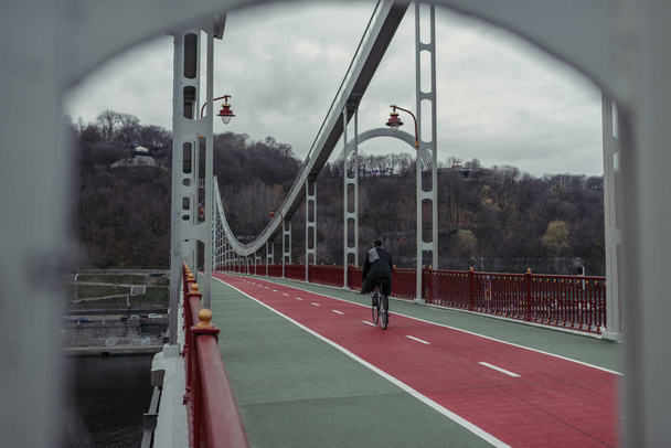 stylish man riding bicycle on pedestrian bridge - Фото, изображение