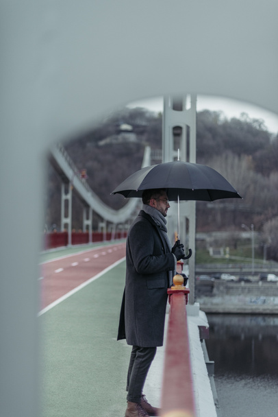 a jóképű felnőtt férfi esernyő állandó híd oldalnézete - Fotó, kép