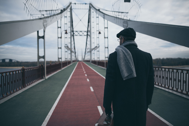 stylish man in coat and scarf with suitcase standing on pedestrian bridge - Foto, afbeelding