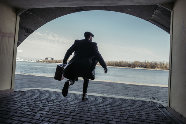 hombre con estilo con la maleta corriendo túnel a la orilla del río
 - Foto, Imagen