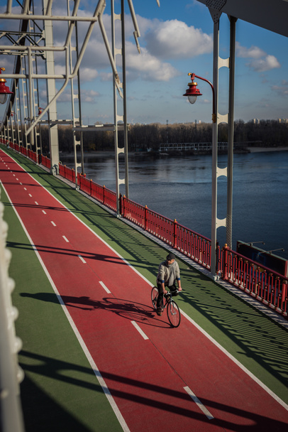 high angle view of adult man riding bicycle on pedestrian bridge over river - Photo, Image