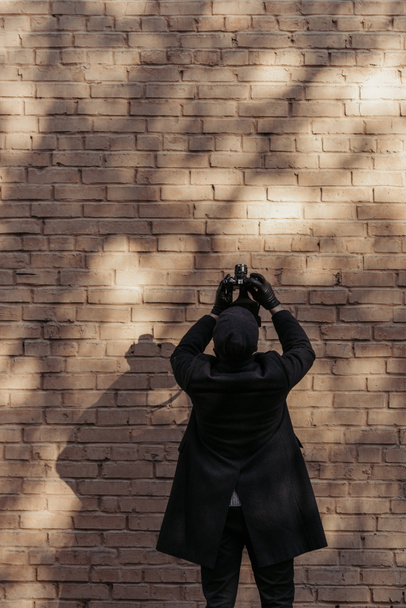 back view of stylish man with camera taking photo of brrick wall - Photo, Image