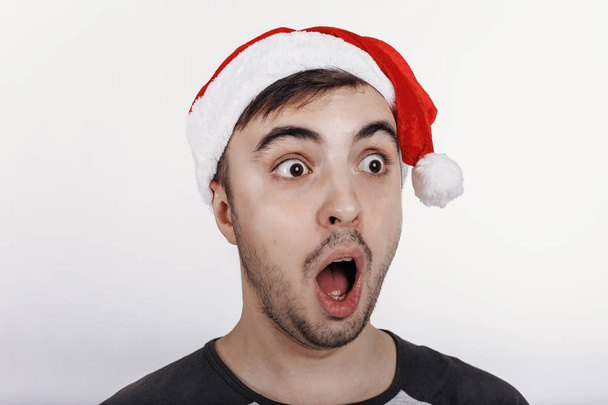 Der junge Mann mit dem Weihnachtsmannhut war von etwas sehr überrascht. Nahaufnahme - Foto, Bild