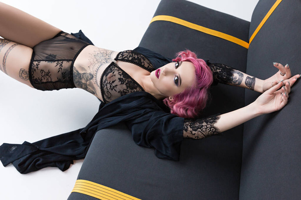 viettelevä tatuoitu vaaleanpunainen tukkainen tyttö läpinäkyvä alusvaatteita poseeraa sohvalla
 - Valokuva, kuva